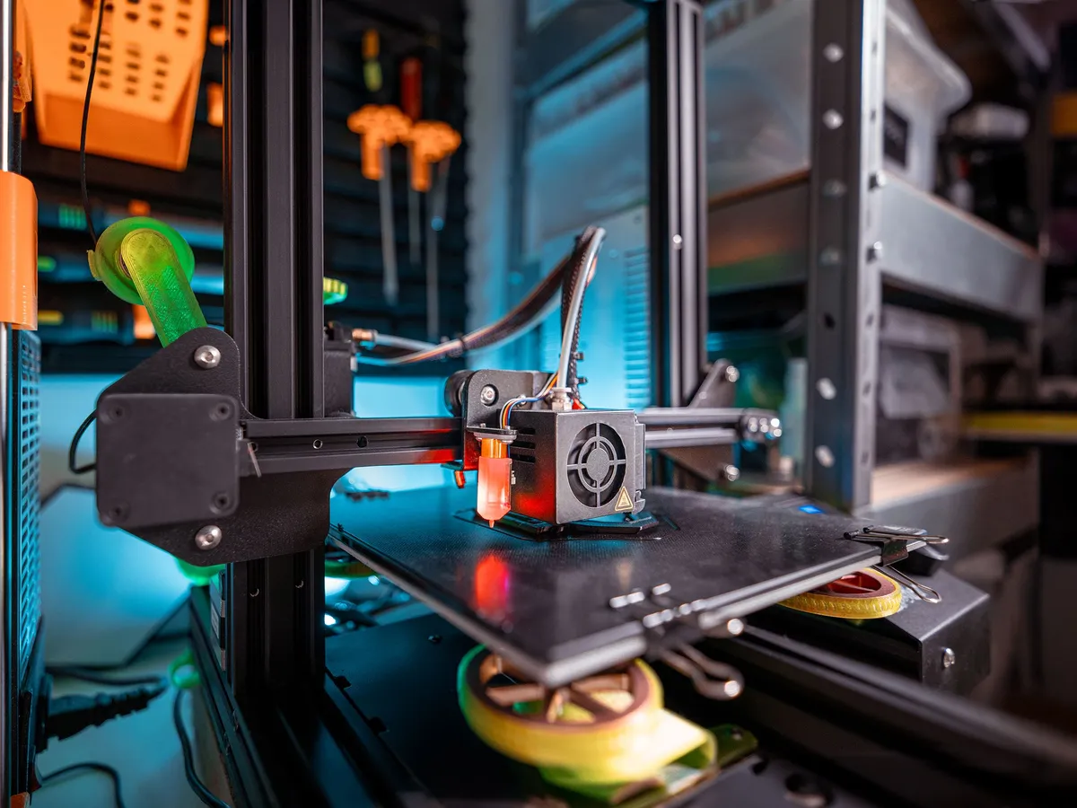 3D printer print head and bed in a workshop with a blue-lit background