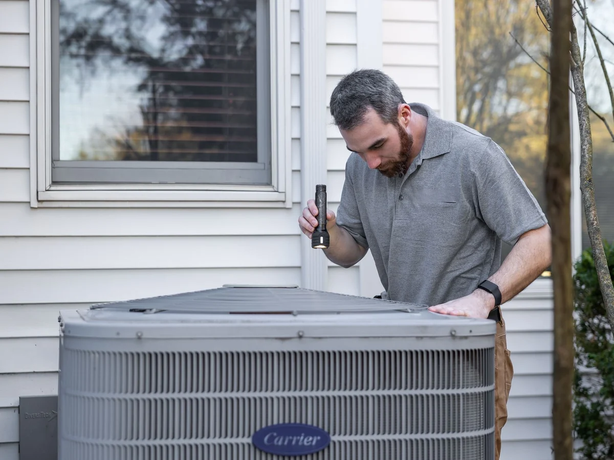 HVAC technician inspecting an outdoor air conditioner condenser beside a house
