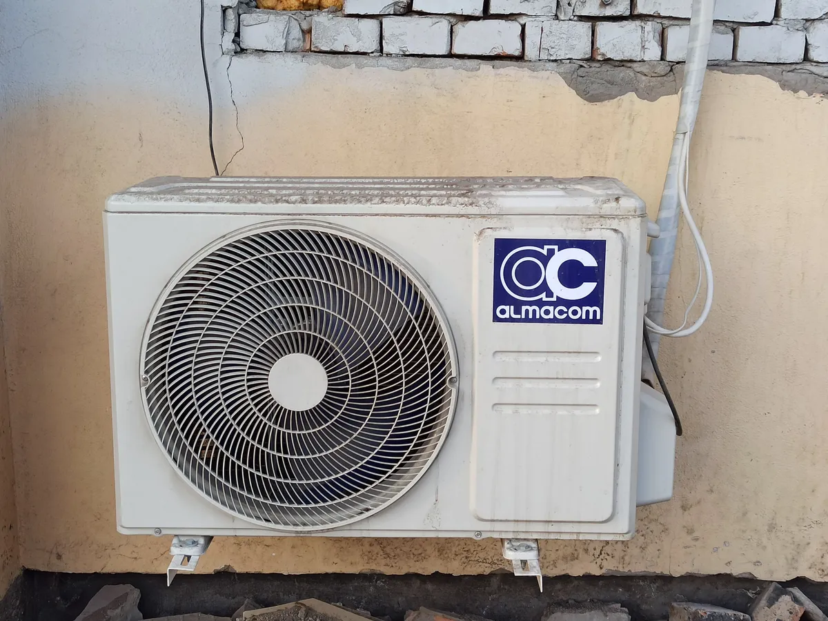Outdoor air conditioner condenser unit with a large fan mounted on a weathered yellow wall