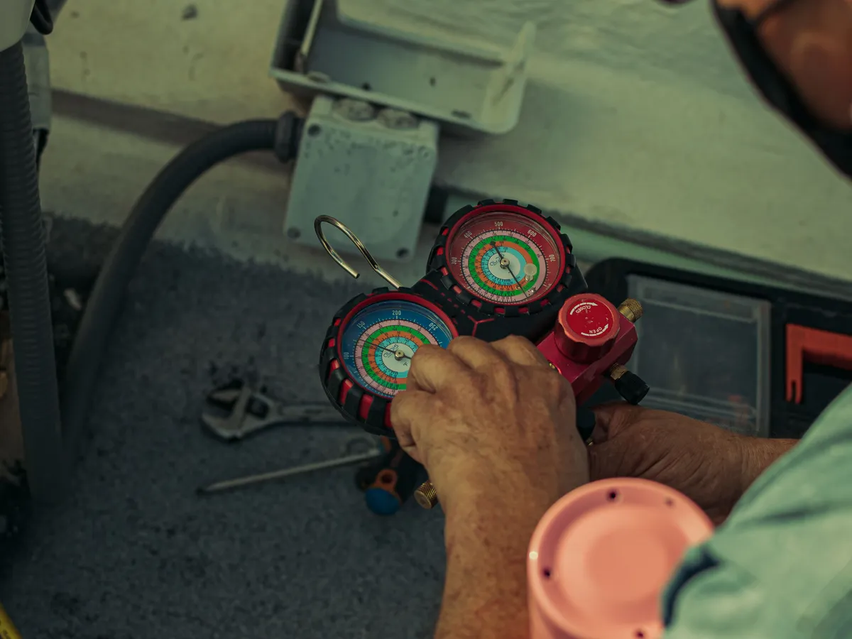 Close-up of a technician's hands adjusting a red refrigerant manifold gauge set