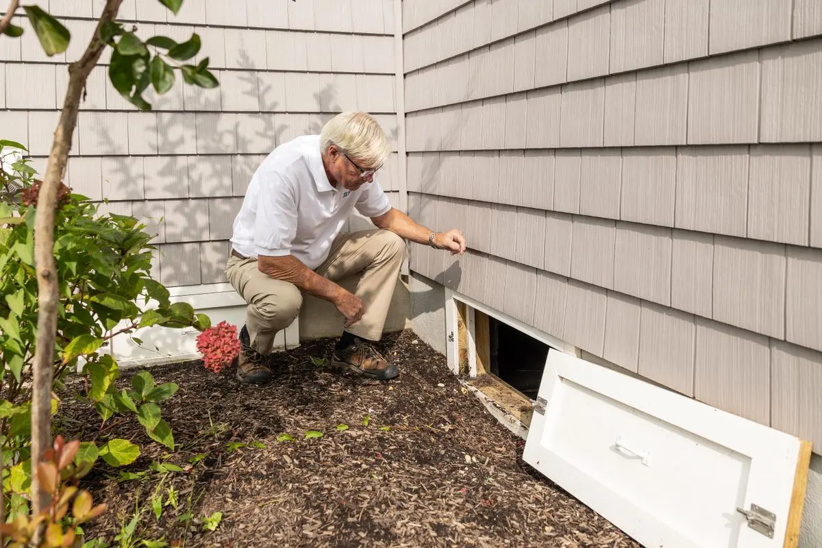Homeowner inspecting the foundation vent and siding at the base of a house