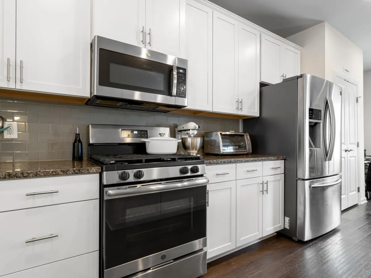 Kitchen with white cabinets, a stainless steel over-the-range microwave, a gas range, a toaster oven and a stainless steel refrigerator
