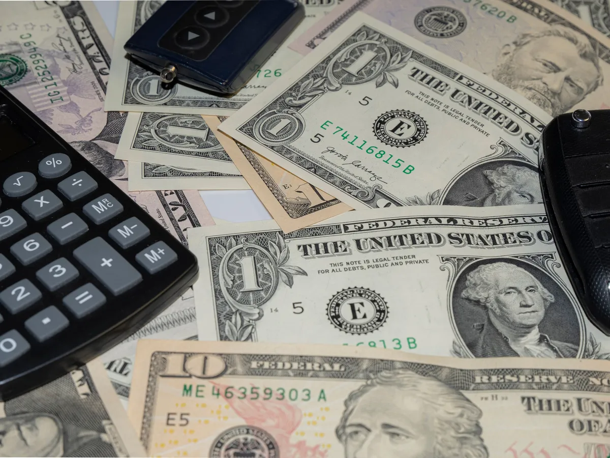 Car keys and a calculator resting on a pile of US dollar bills