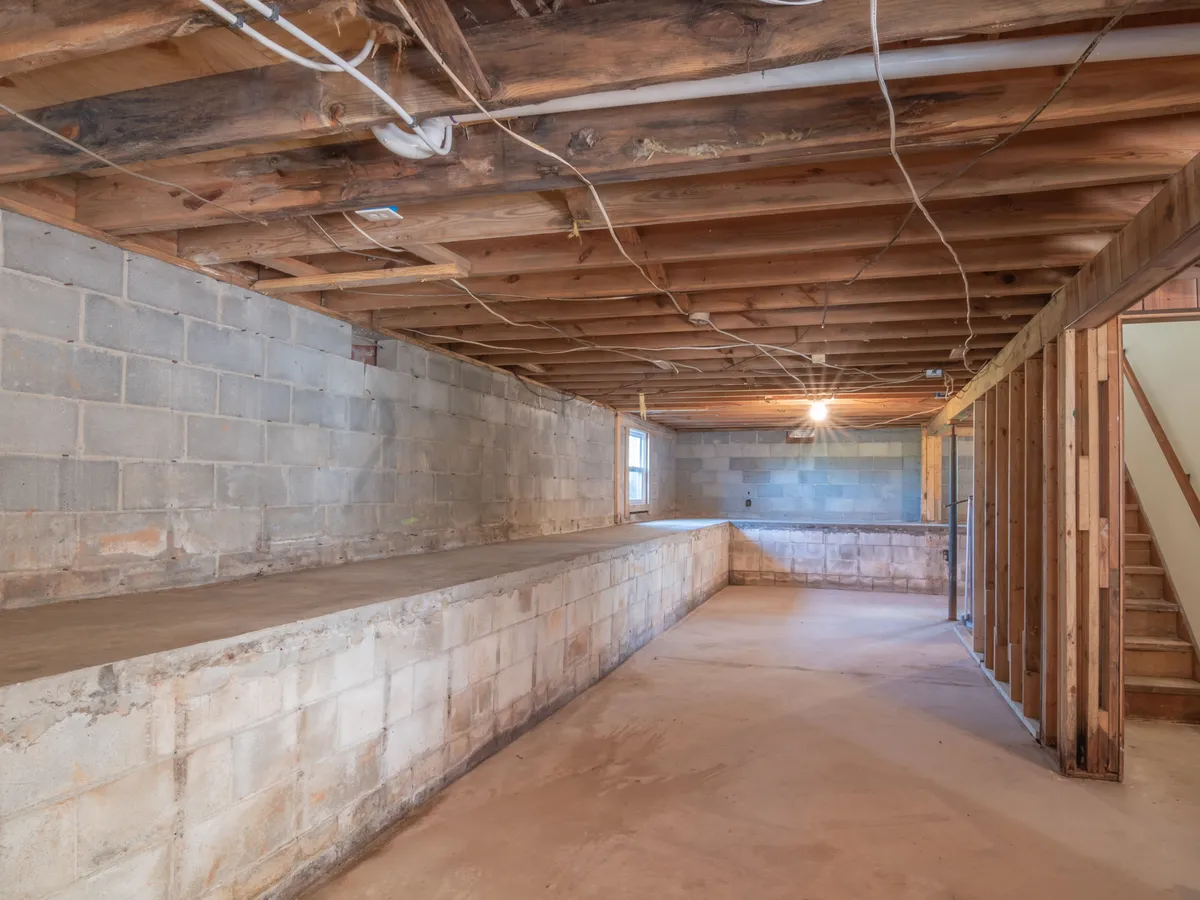 Unfinished basement with concrete block walls, exposed floor joists and a bare concrete floor