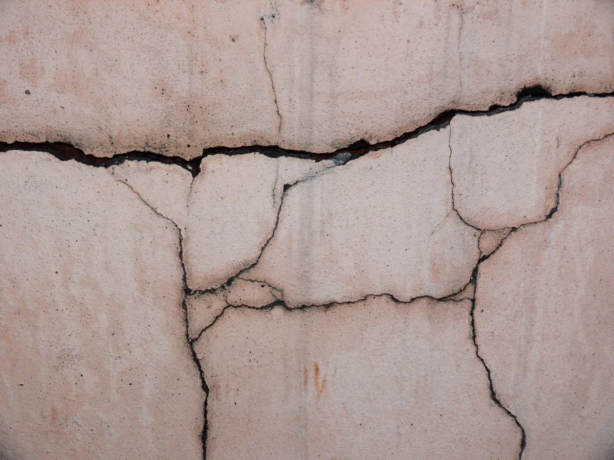 Close-up of a cracked pink-tinted concrete wall with a wide horizontal crack and several branching hairline cracks