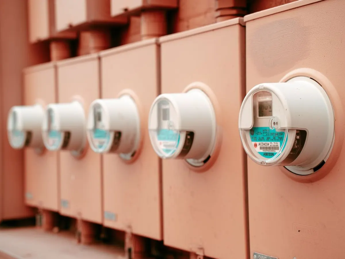 Row of five white residential electricity meters mounted on pink-beige metal enclosures along an exterior wall