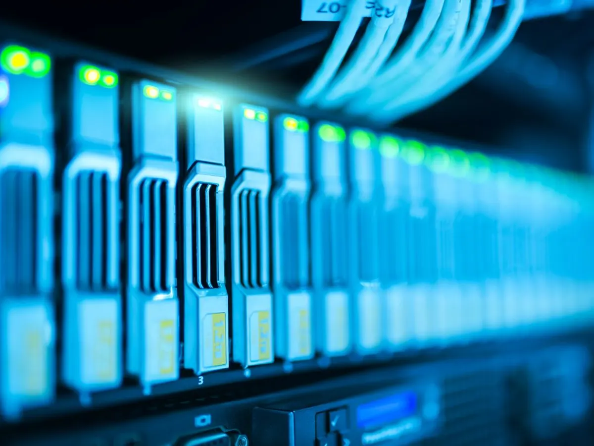 Close-up of a rack of server units with glowing green status lights and network cables, similar to hardware used in mining facilities