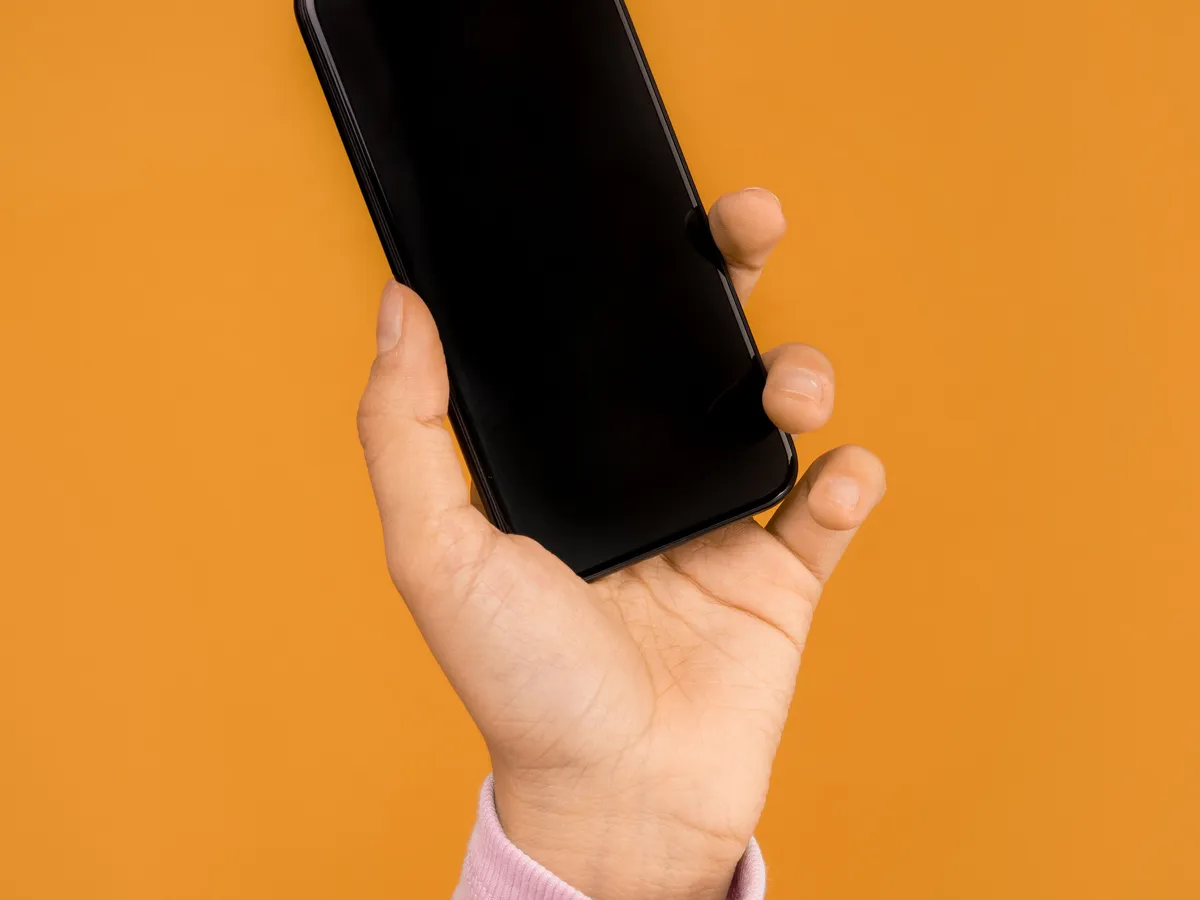 Hand holding up a black smartphone against an orange background