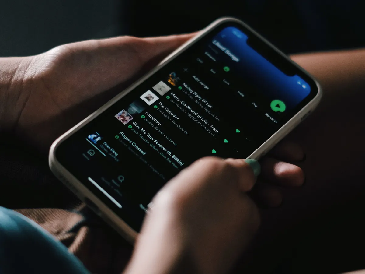 Two hands holding a smartphone showing a music app in a dim room
