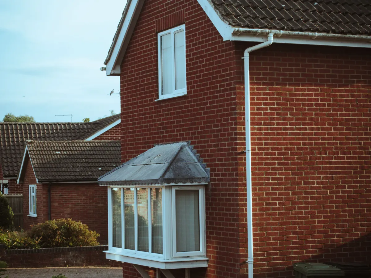Red brick house with a white-framed bay window on the ground floor and a casement window above