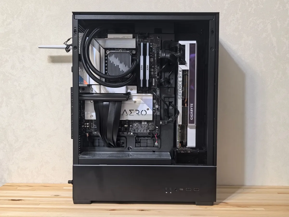 Open-sided PC case showing a GeForce RTX graphics card, liquid cooler and motherboard on a wooden desk