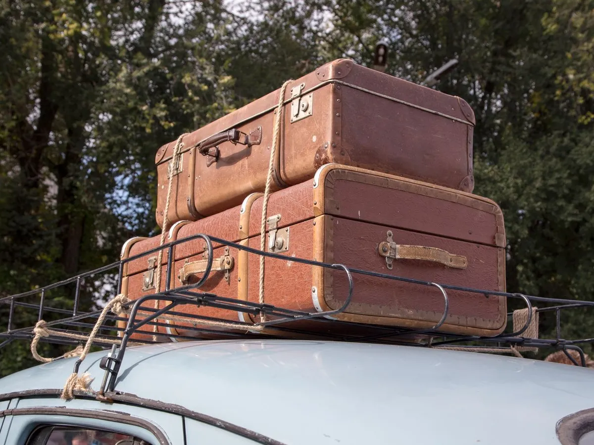 Vintage suitcases stacked on a classic car roof rack parked on a mountain road