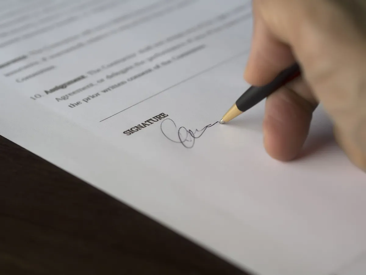 Hand signing a contract with a pen on a printed document