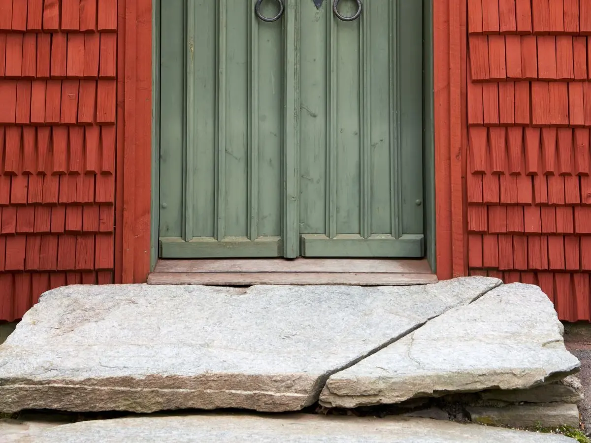 Weathered green wooden front door with a stone step