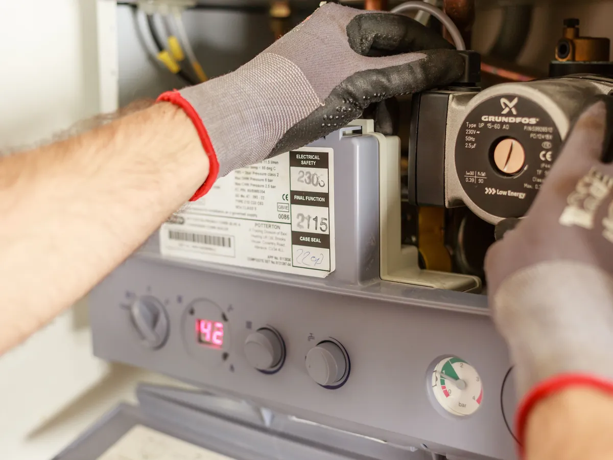 Gloved technician servicing the controls and circulation pump of a wall-mounted heating unit