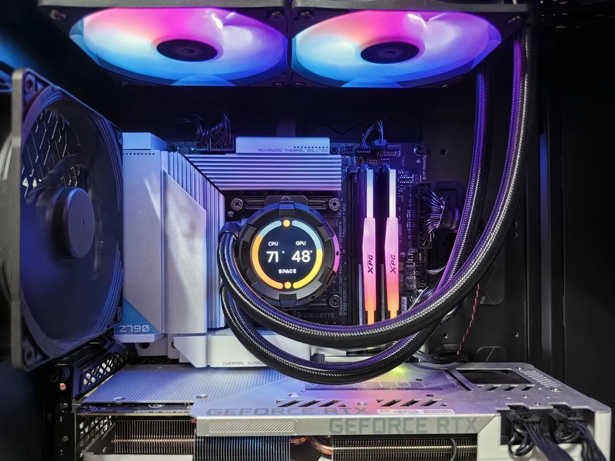 Inside of a gaming PC with RGB fans, liquid cooler with a temperature display, RAM sticks and a GeForce RTX graphics card