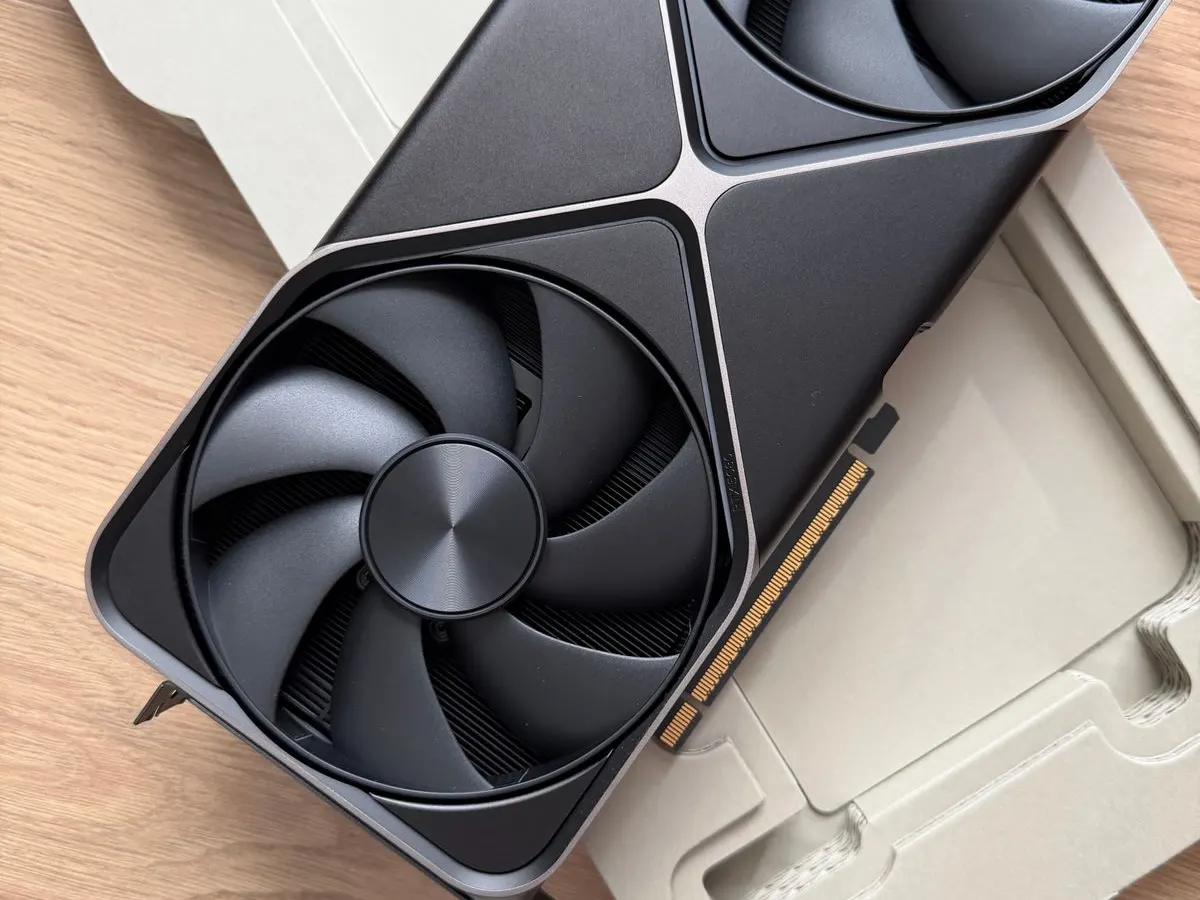Close-up of a dark gray RTX-class graphics card with a large cooling fan and gold PCIe connector on a wooden table