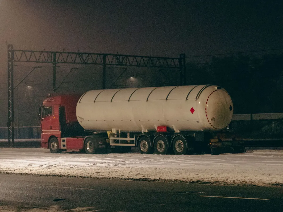 Red fuel tanker truck parked on a snowy road at night