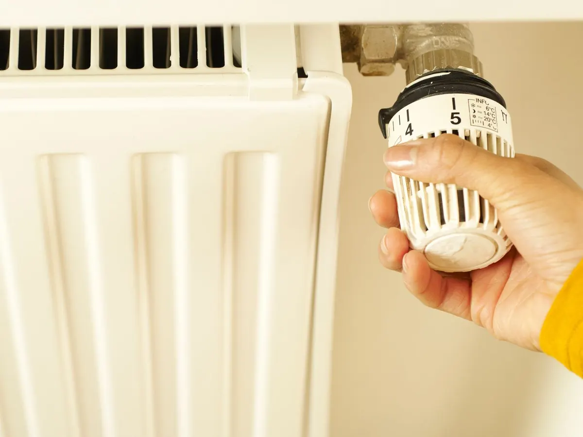 Hand turning a radiator thermostat valve on a white radiator