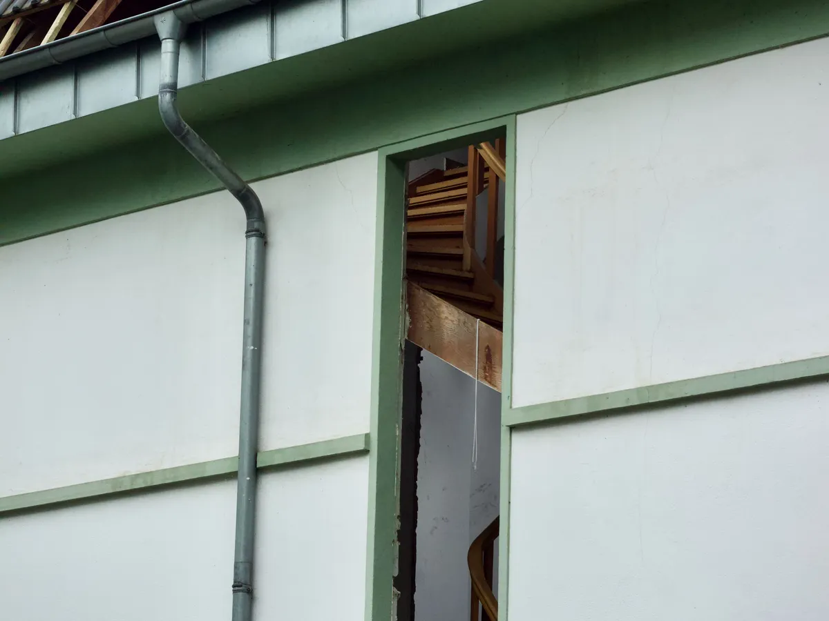 House exterior with an open wall section and unfinished roof edge showing the staircase inside
