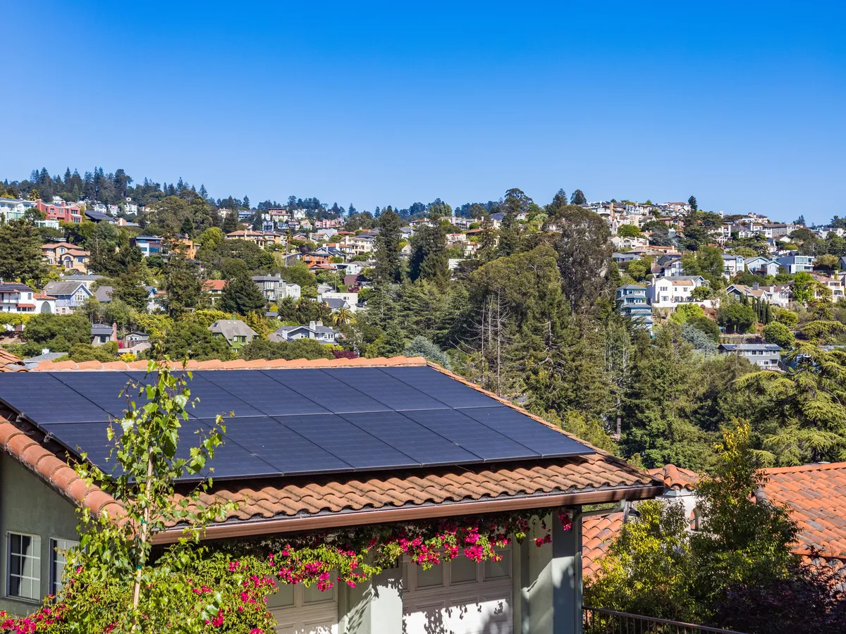 Rooftop solar array on a tile-roofed house in a hillside neighborhood under a clear blue sky