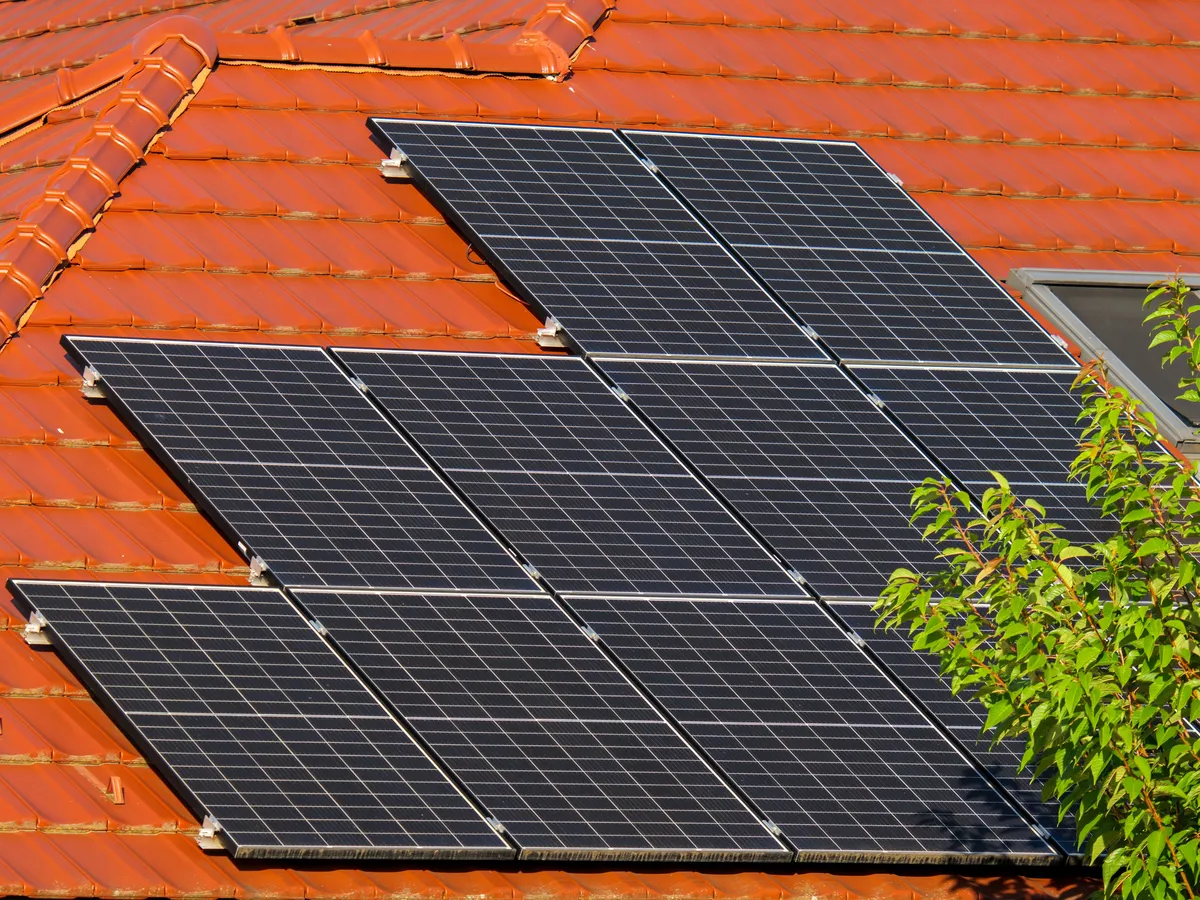 Close-up of eleven dark solar panels mounted on an orange clay tile roof next to a skylight