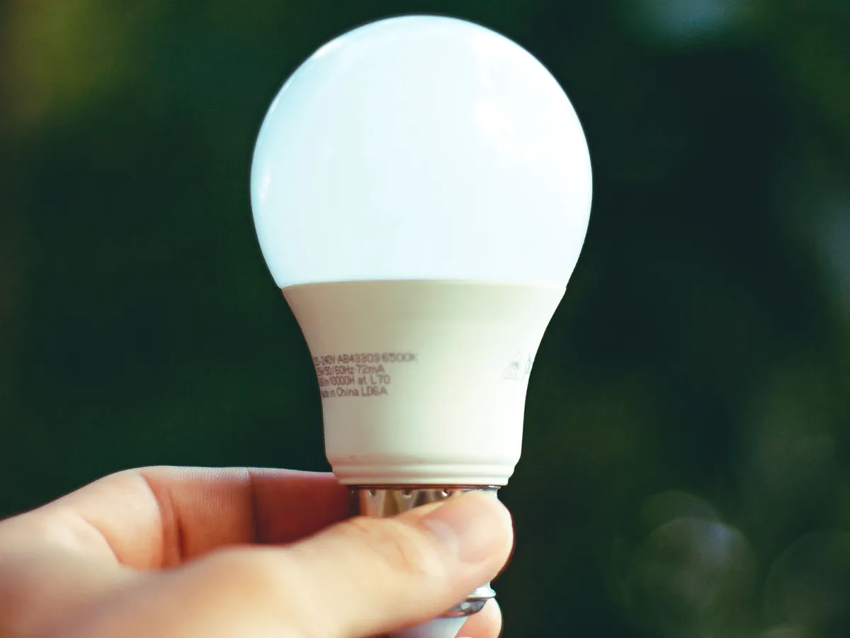 Hand holding a lit white LED light bulb against a dark green blurred background