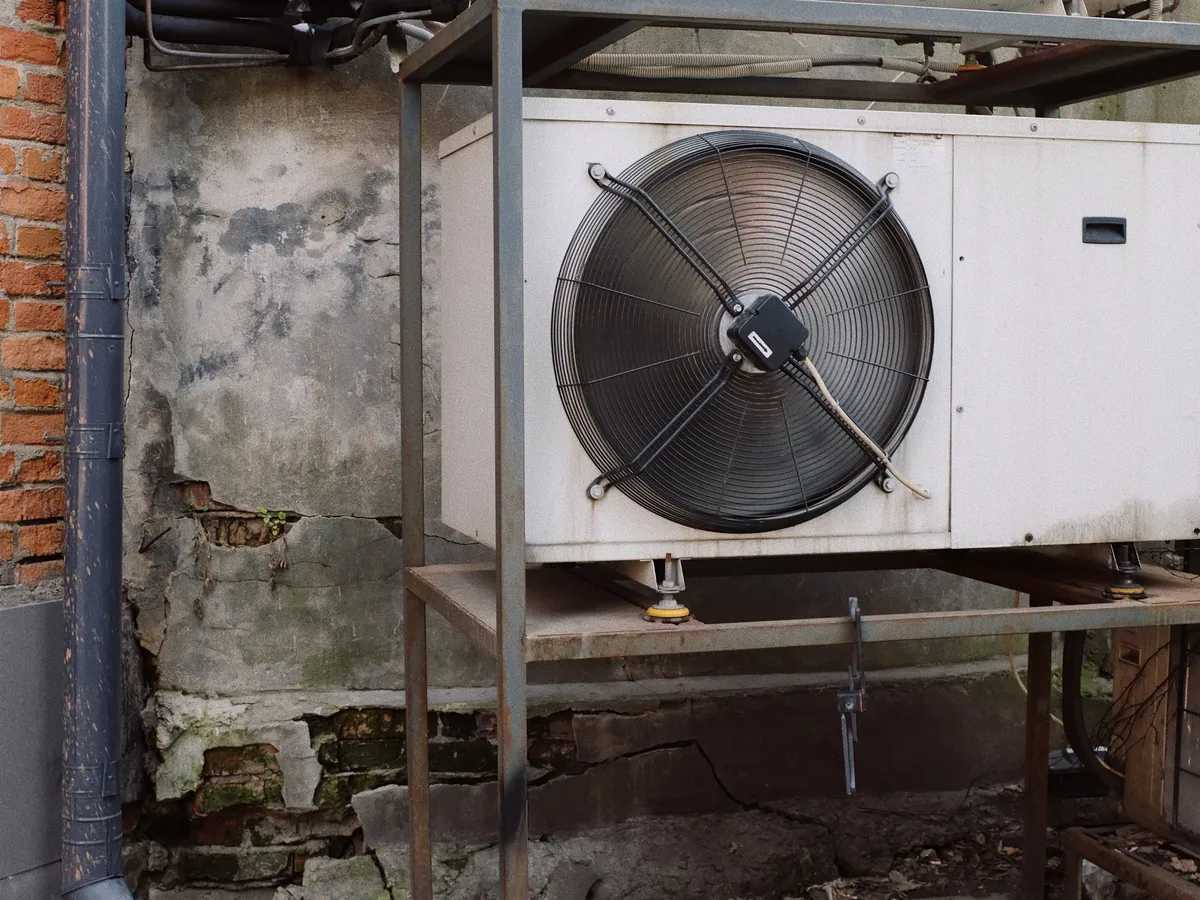 Old outdoor air conditioner condenser mounted on a metal rack against a weathered brick wall