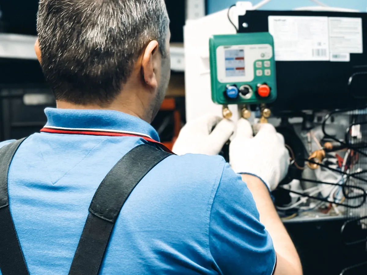 HVAC technician in a blue shirt connecting a digital manifold gauge to a system's service ports