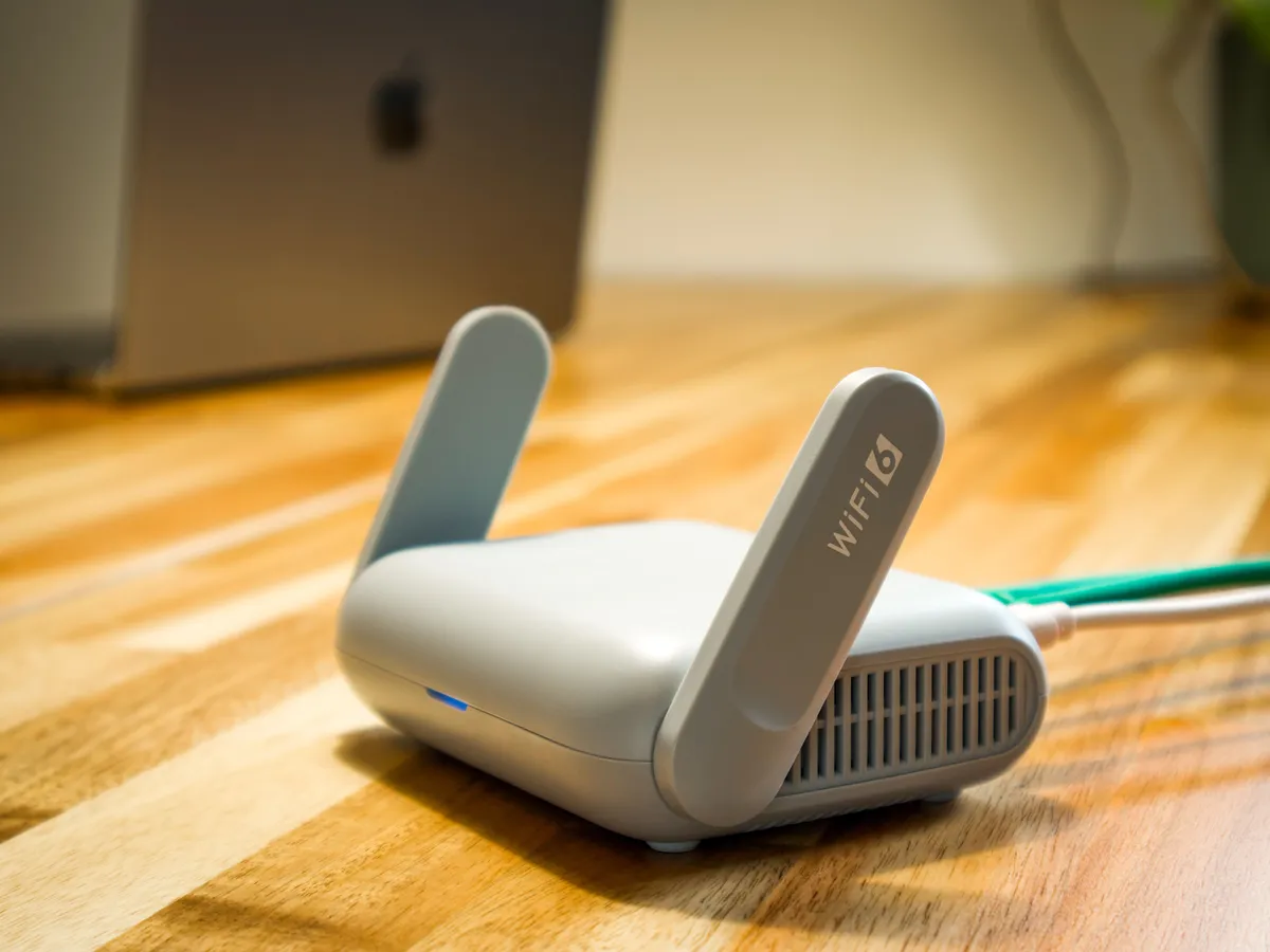 Compact white Wi-Fi 6 travel router on a wooden floor next to a laptop