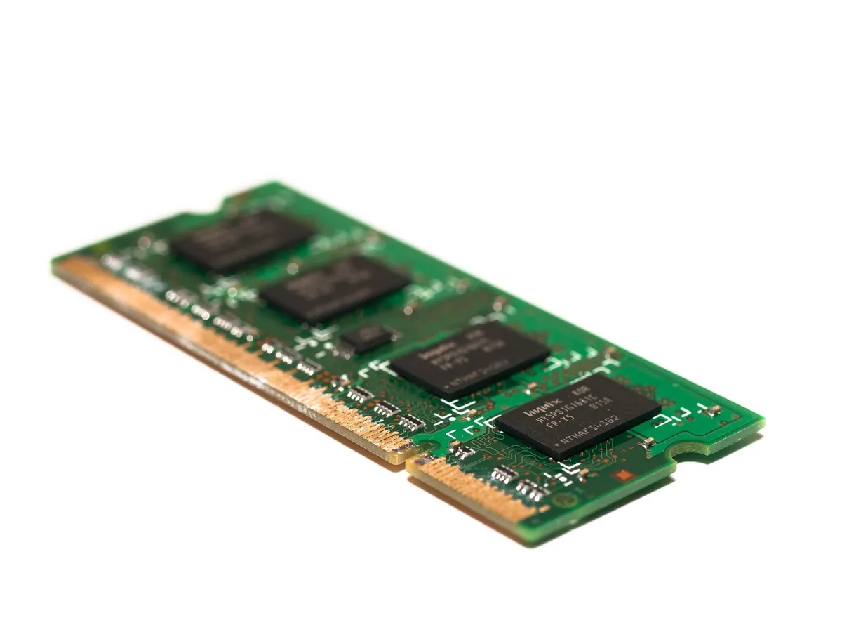 Close-up of a green laptop memory module with four black DRAM chips against a white background