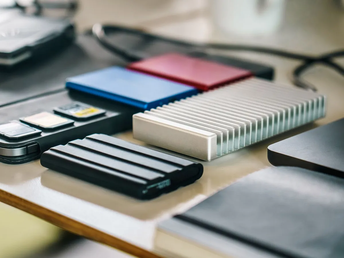 Portable solid-state drives in blue, red, silver and black laid out on a desk next to memory cards