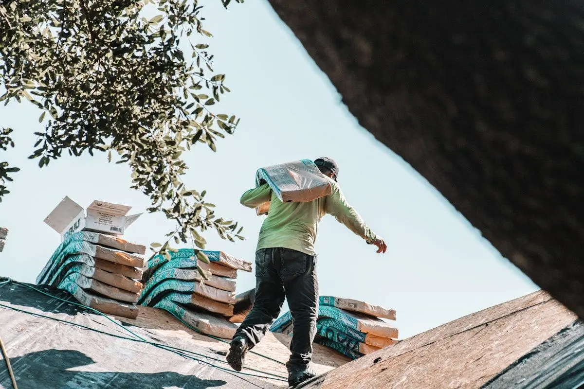Roofer hauling bundles of new shingles onto a roof