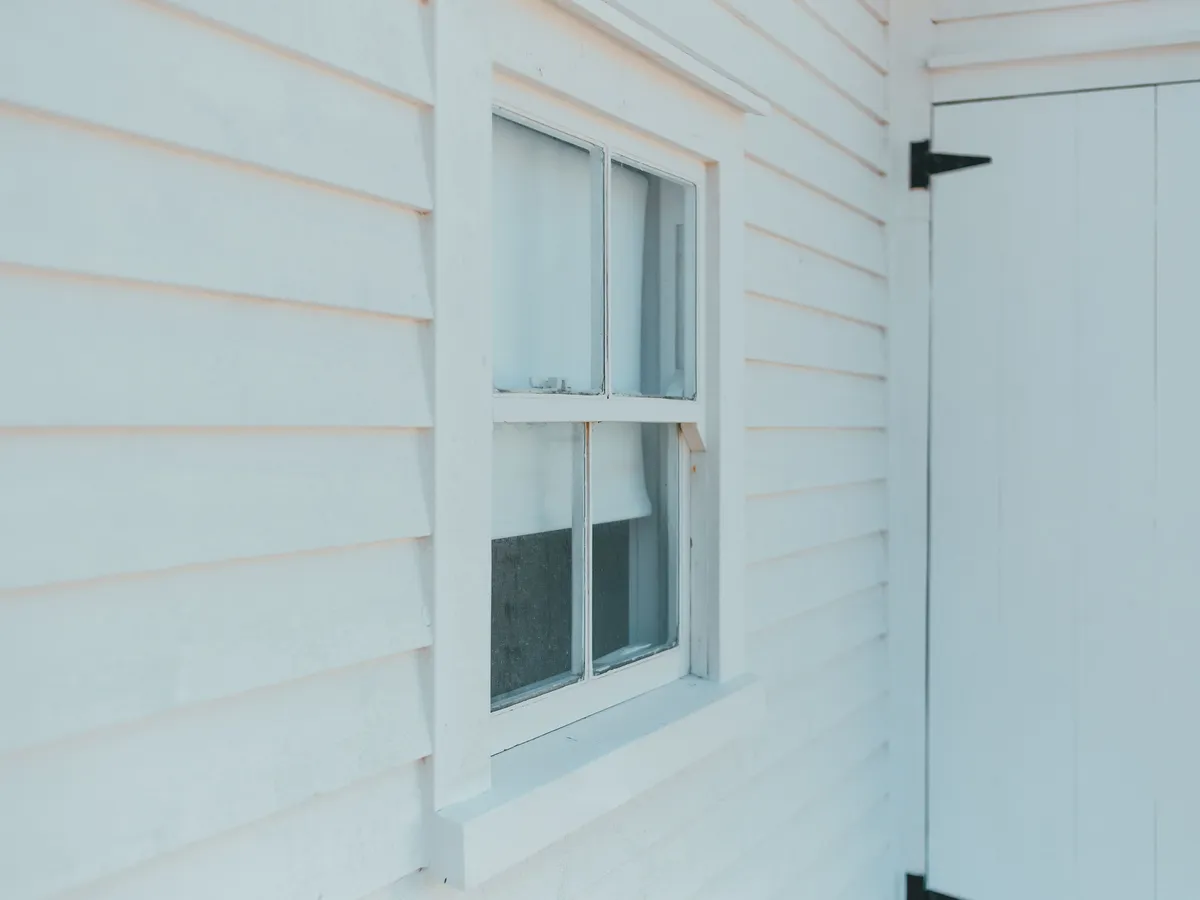 White horizontal lap siding around a double-hung window and a white board door with black hinge