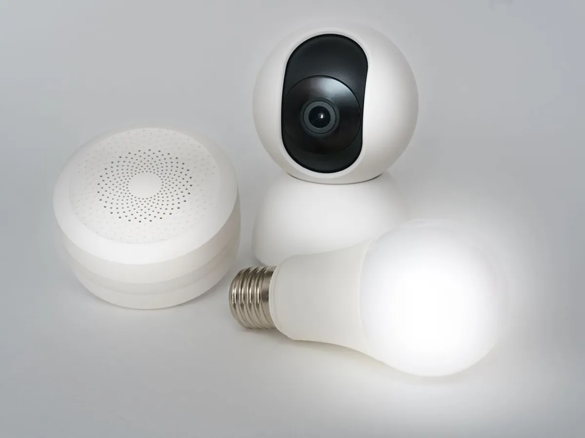 White pan-tilt indoor camera, round white hub and a lit smart bulb on a gray background