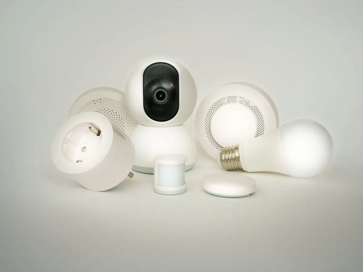 Smart plug, pan-tilt camera, motion sensor, hub and a lit bulb arranged together on a gray background
