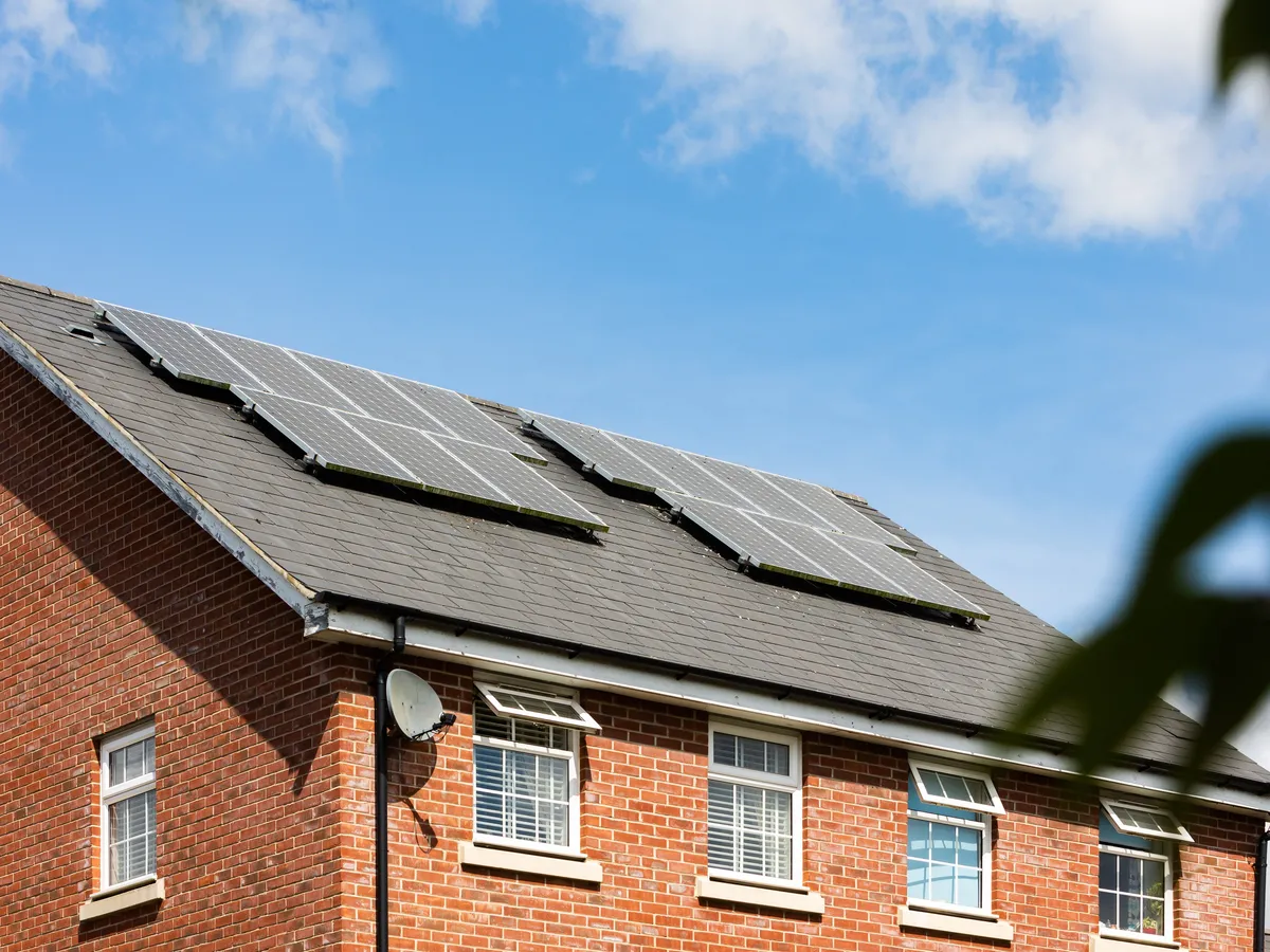 Brick house with grey slate roof carrying two groups of solar panels under a blue sky