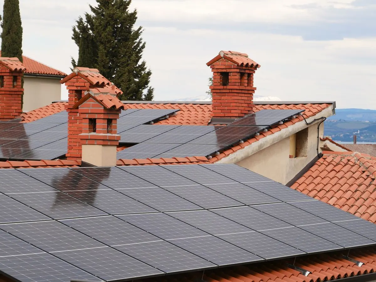 Solar panels on a terracotta roof between brick chimneys with distant hills and sea in the background