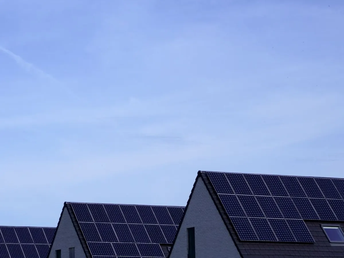 Row of houses with dark solar panels covering their roof slopes under a clear blue sky