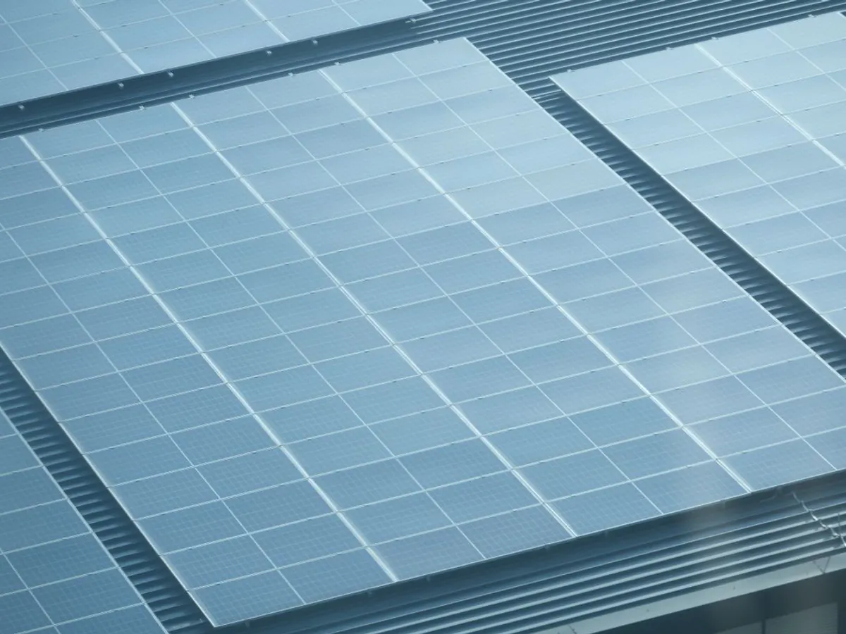 Dark solar panels installed on an orange tile roof beside two skylight windows and a solar thermal collector