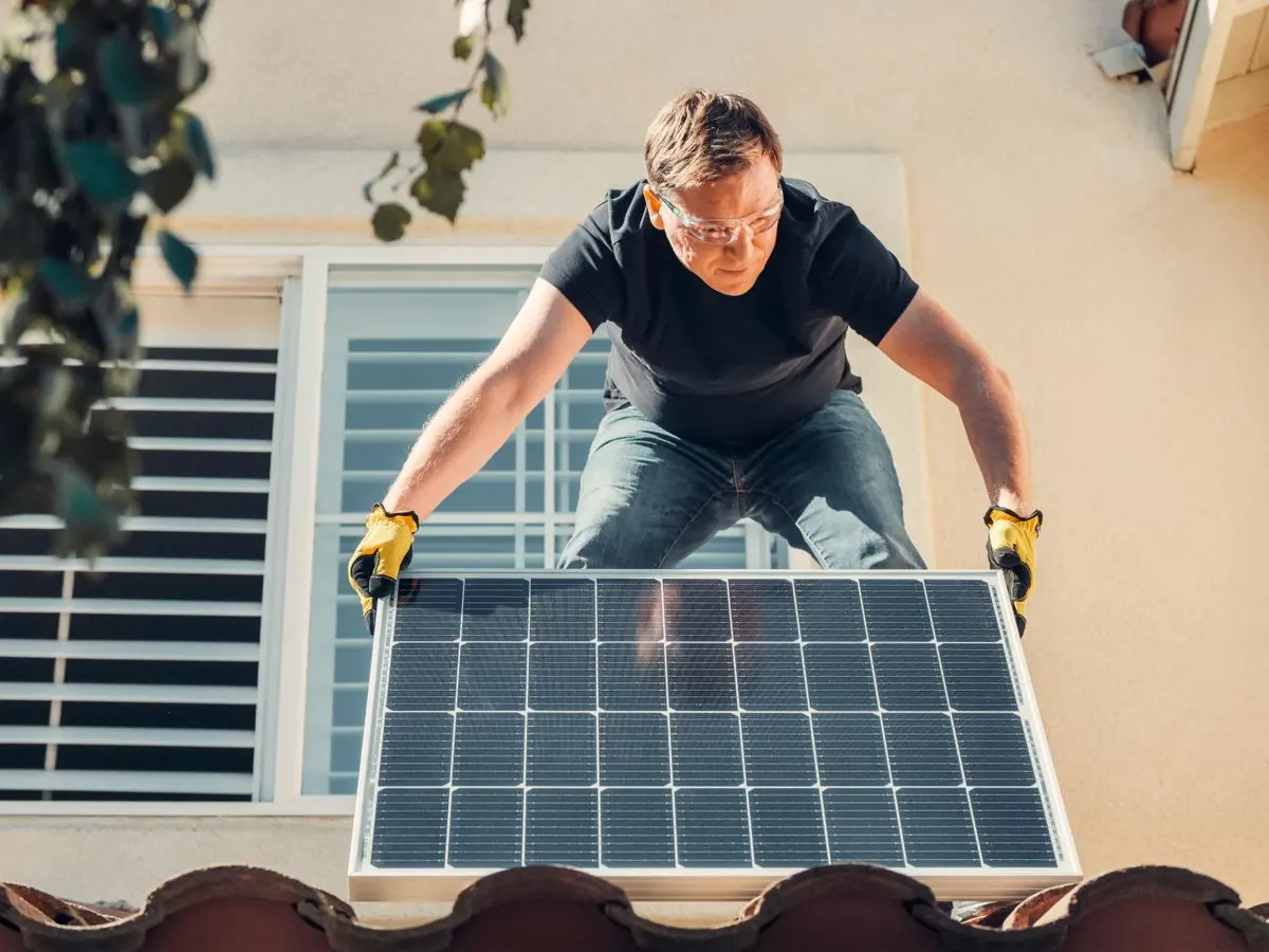 Installer carrying a solar panel onto a tile roof