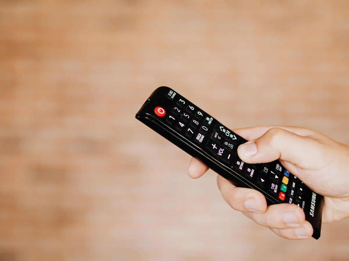 Hand holding a black remote control pointed at a television
