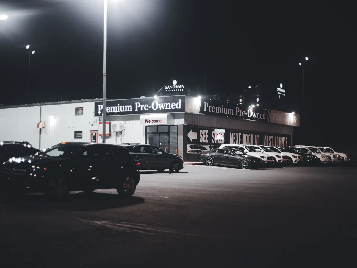 Row of pre-owned cars lit up on a dealership lot at night