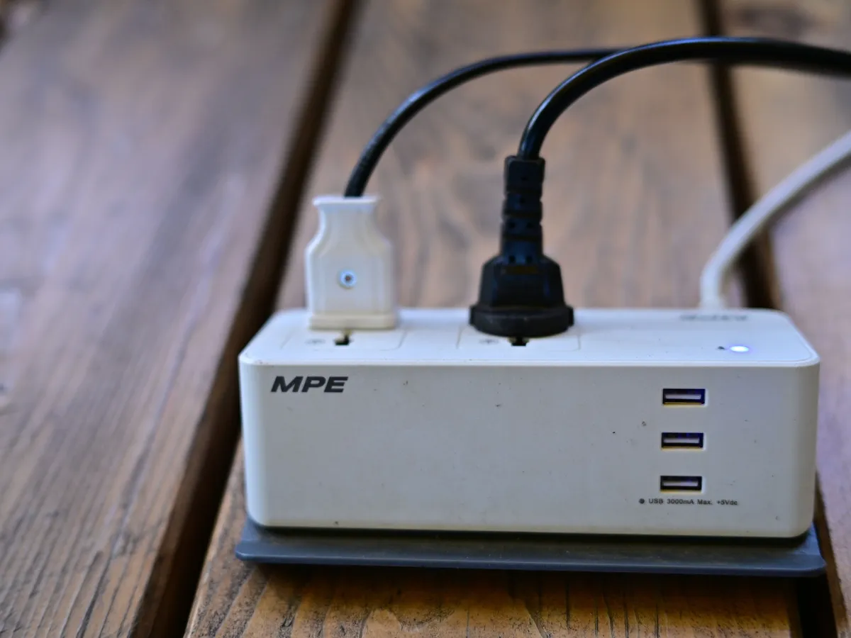 White power strip with USB ports on a wooden surface with two plugs connected and an indicator light lit