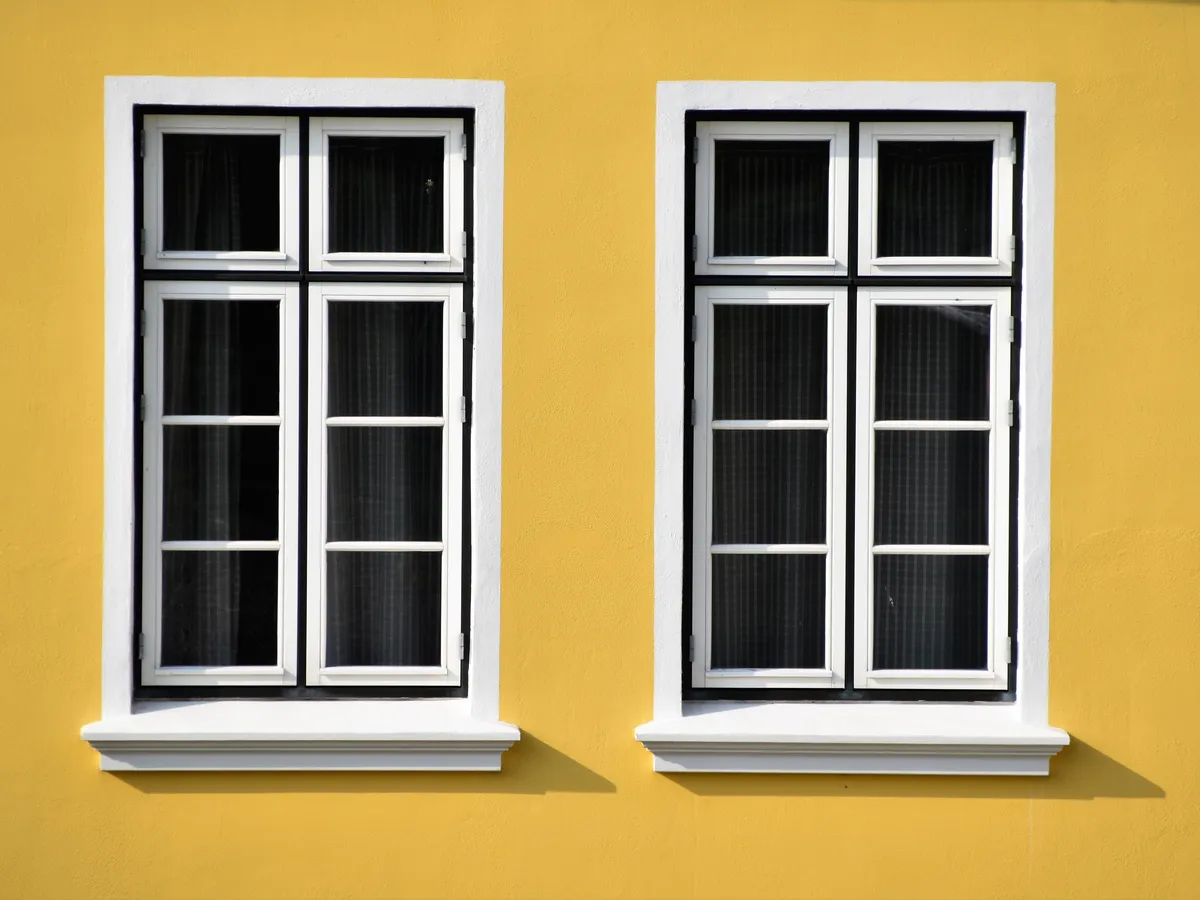 Two white-framed casement windows with black interior trim on a bright yellow wall