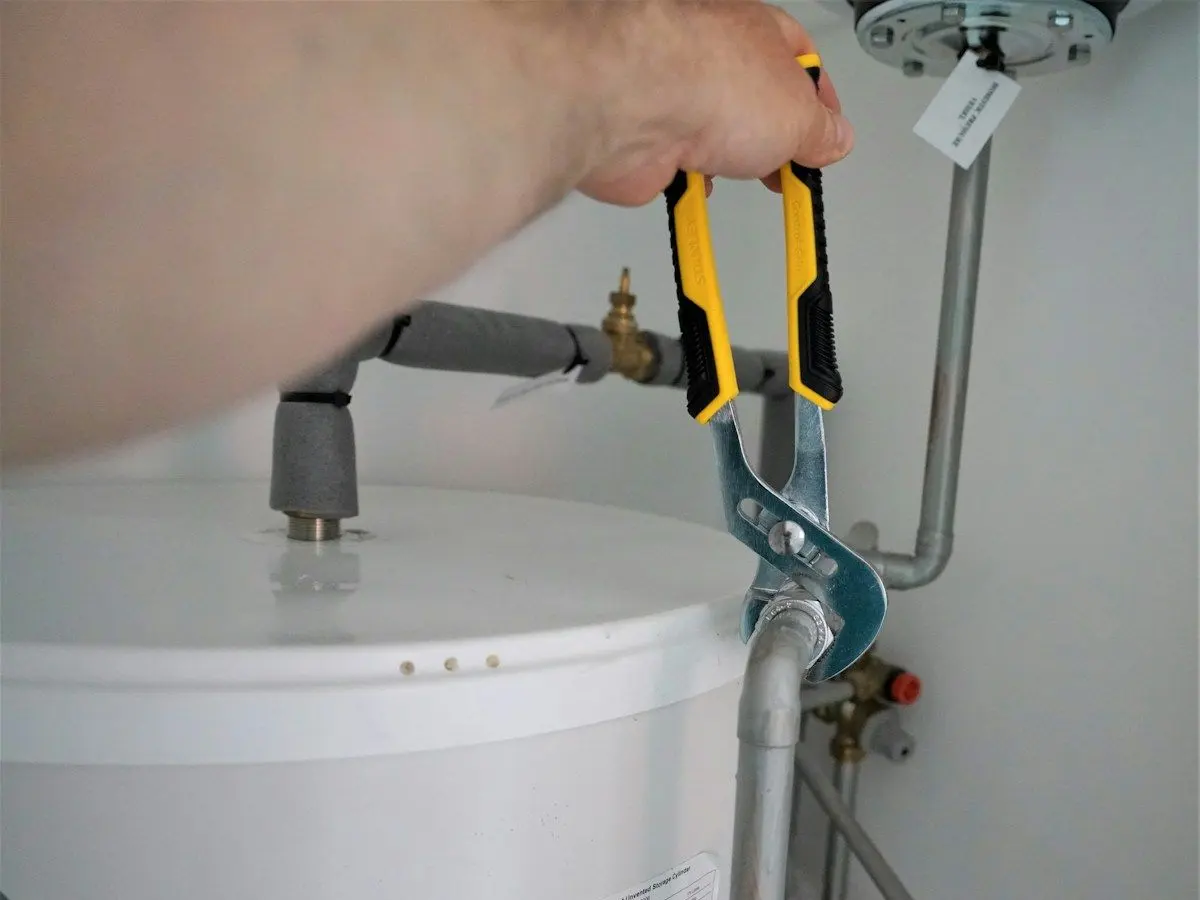 Plumber tightening a fitting on a tank water heater supply line