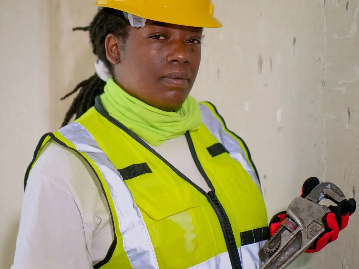 Plumber in a hard hat and safety vest holding a pipe wrench