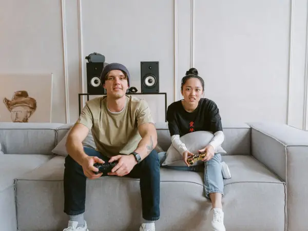 Couple playing video games together on a gray couch in a bright living room